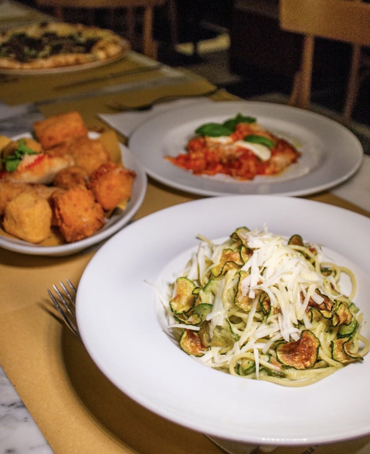Spaghetti alla Nerano con zucchine e provolone, con fritti e parmigiana sullo sfondo