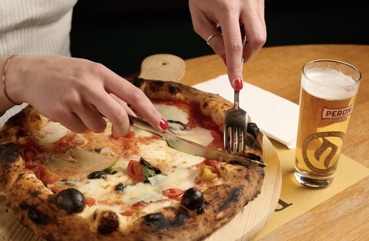 Pizza tagliata su tagliere di legno con birra alla spina