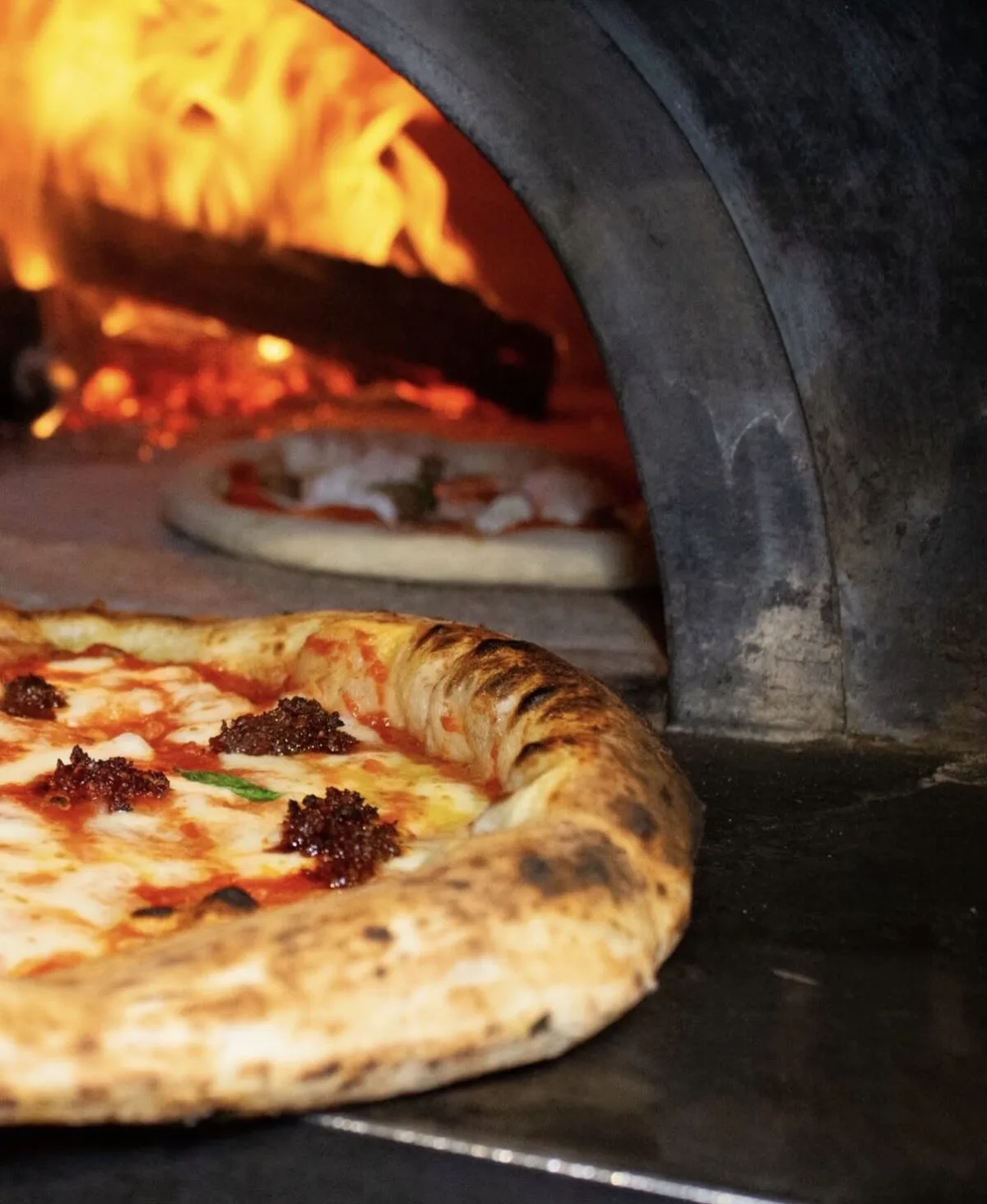 Pizza ’Nduja appena sfornata davanti alla bocca del forno a legna acceso